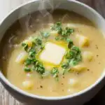 Creamy old-fashioned potato soup in a white ceramic bowl with parsley and butter on top, served on a rustic wooden table.