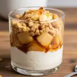 The Best Baked Apple Crumble With Sweet Cinnamon Cream 3 Glass filled with layers of creamy cinnamon mousse, tender baked apple chunks, and golden crumble topping with almond flakes on a wooden table.